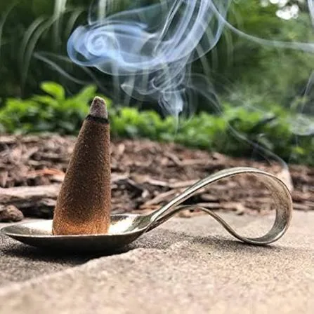 Herbal dhoop cone smouldering on a brass spoon holder